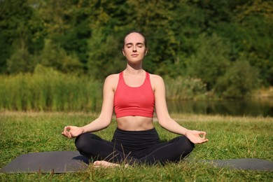 Beautiful woman practicing yoga on mat outdoors. Lotus pose