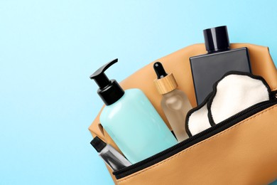 Photo of Preparation for spa. Compact toiletry bag with different cosmetic products on light blue background, top view. Space for text