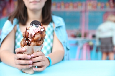 Photo of Young woman holding delicious sweet bubble waffle with ice cream at table outdoors, closeup