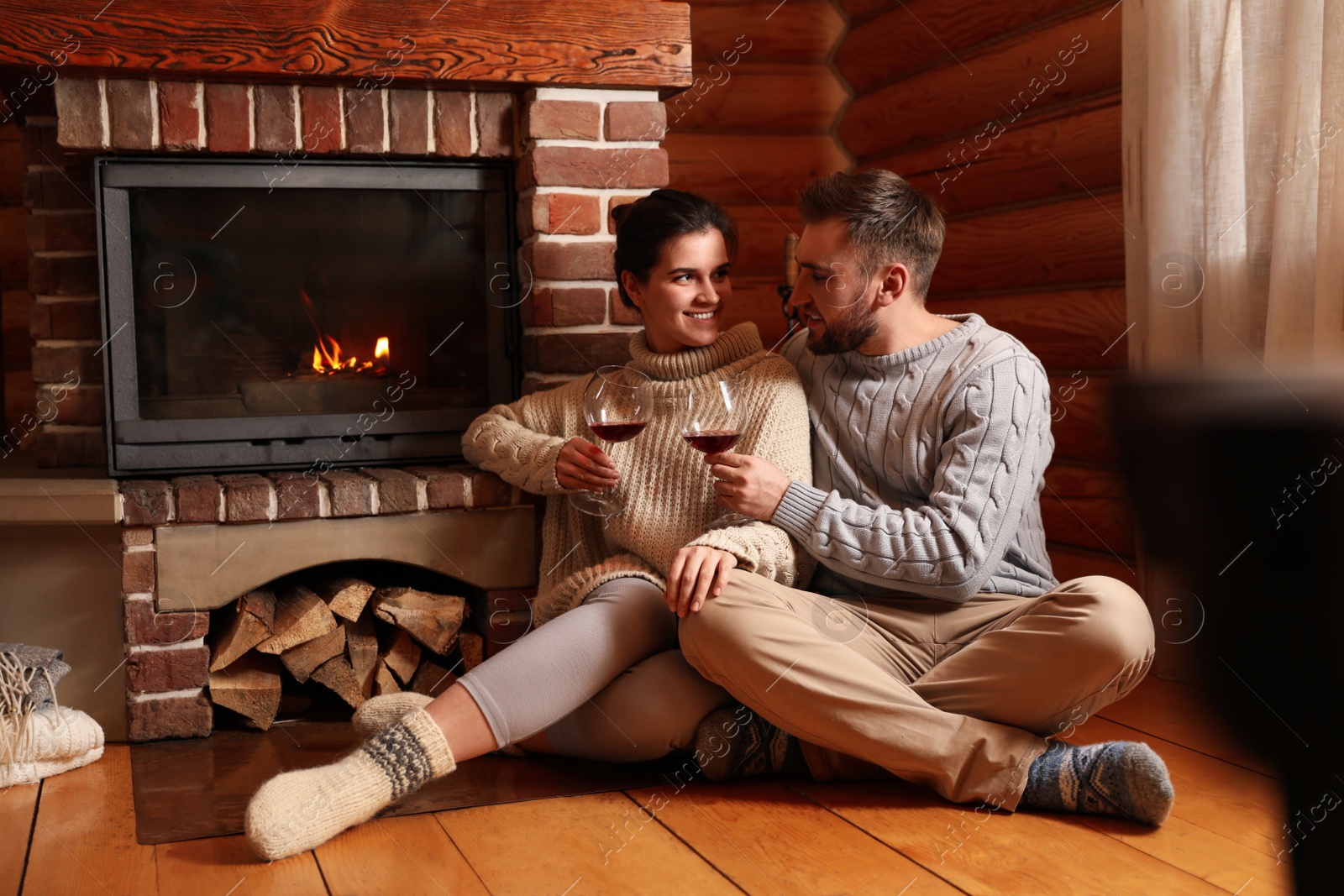 Photo of Lovely couple with glasses of wine near fireplace at home. Winter vacation