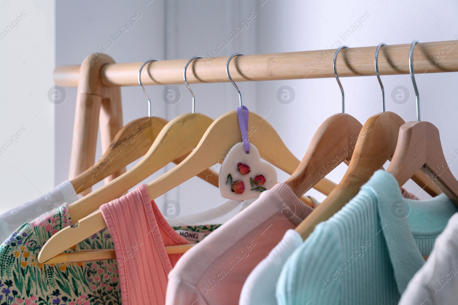 Photo of Beautiful scented wax sachet and clothes hanging on wooden rack indoors