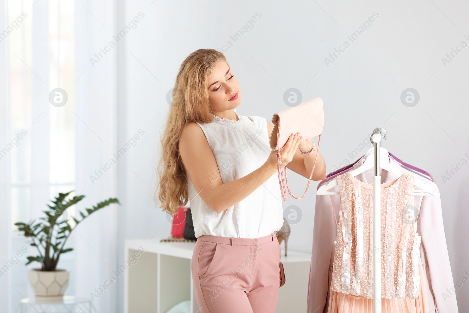 Photo of Young woman holding stylish purse near rack with clothes in boutique