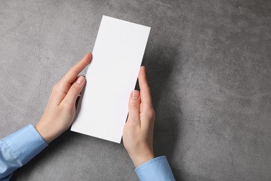 Photo of Woman holding blank card at grey table, top view. Mockup for design