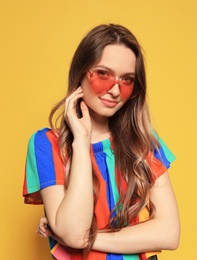 Photo of Portrait of beautiful young woman with heart shaped sunglasses on color background