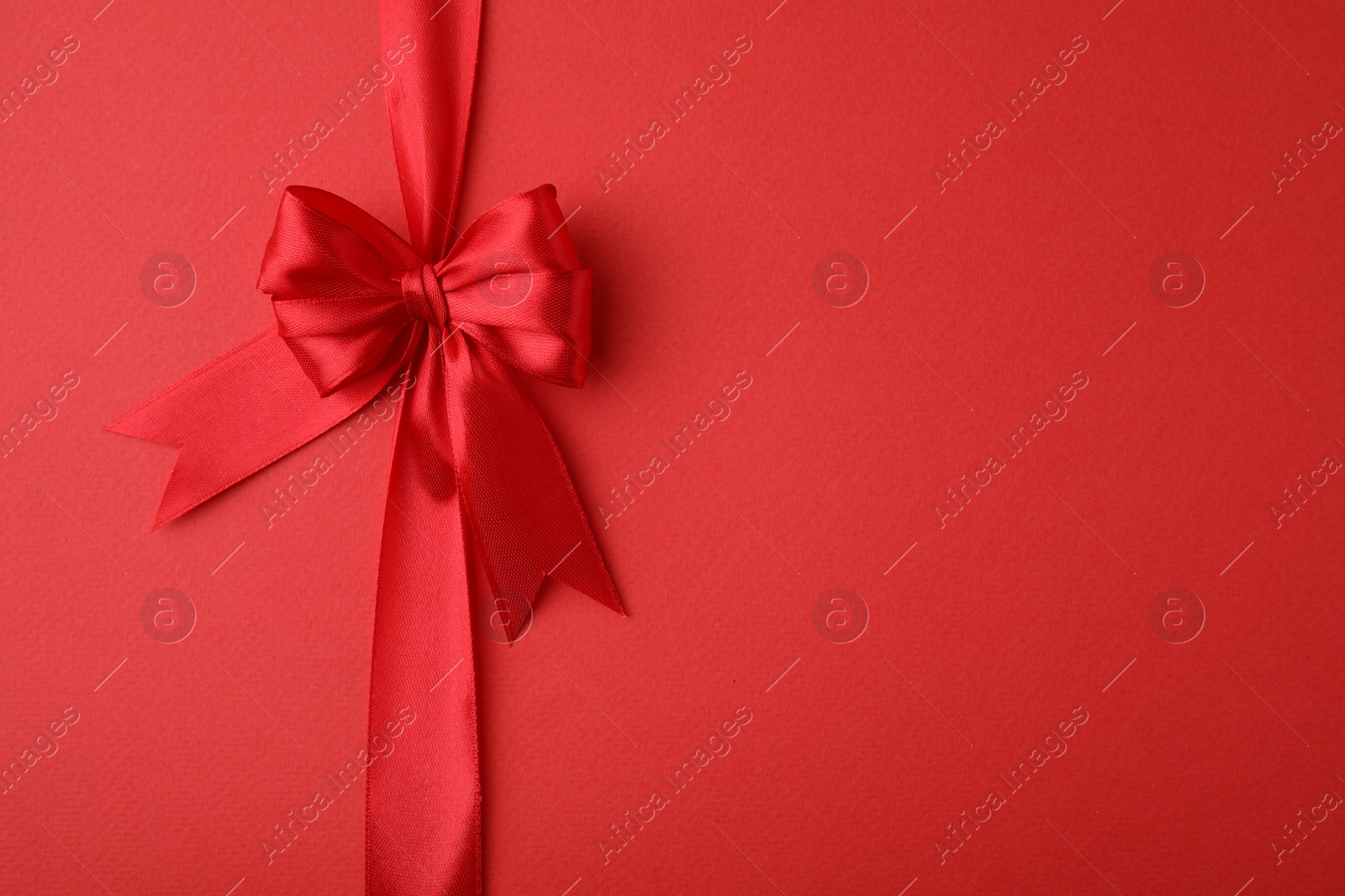 Photo of Bright satin ribbon with bow on red background, top view. Space for text