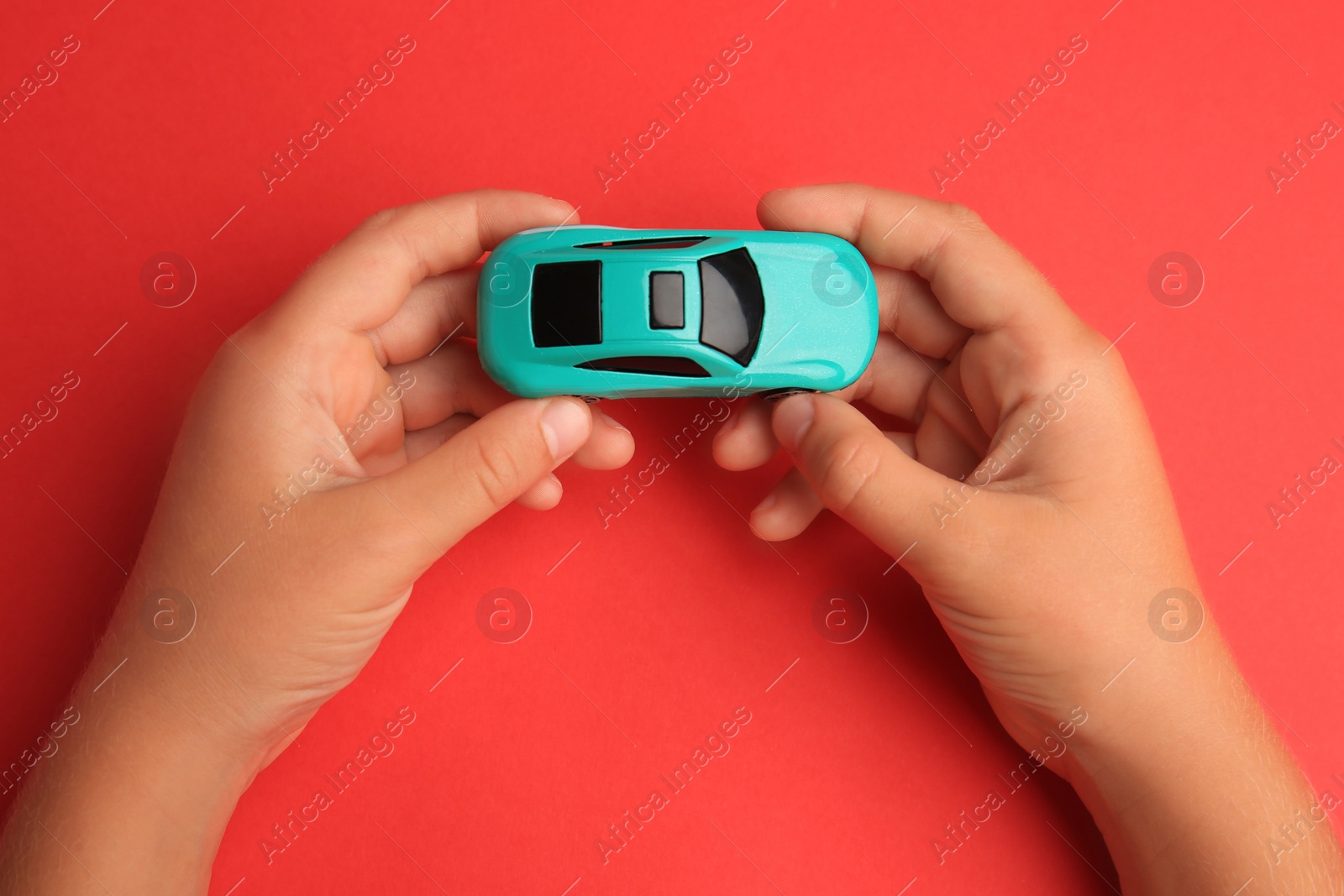 Photo of Child holding toy car on red background, top view