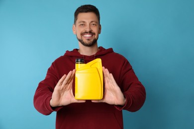 Photo of Man showing yellow container of motor oil on light blue background