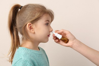 Photo of Mother helping her daughter to use nasal spray on beige background