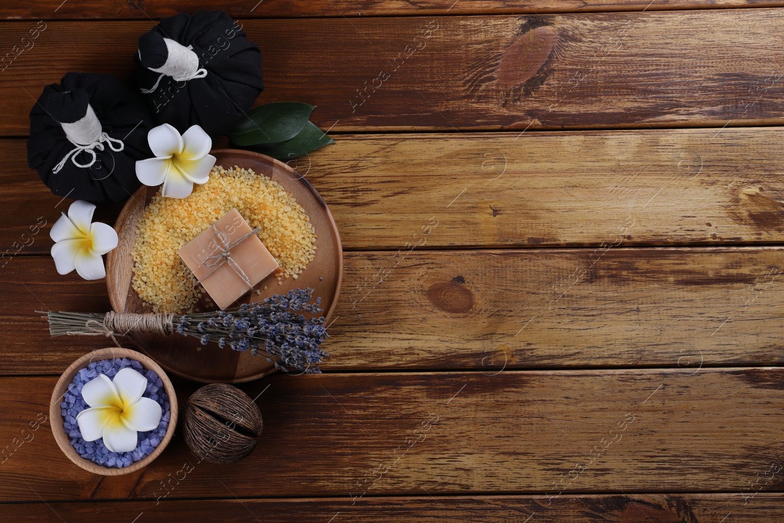 Photo of Spa composition. Sea salt, soap bar, herbal bags and flowers on wooden table, flat lay. Space for text