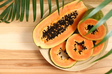 Plate with cut papayas on wooden table, top view. Space for text