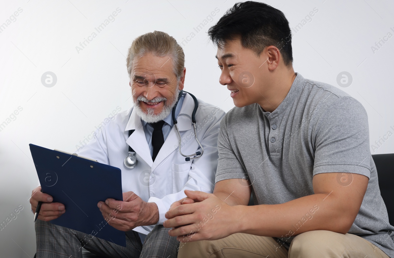 Photo of Senior doctor with clipboard consulting patient in clinic