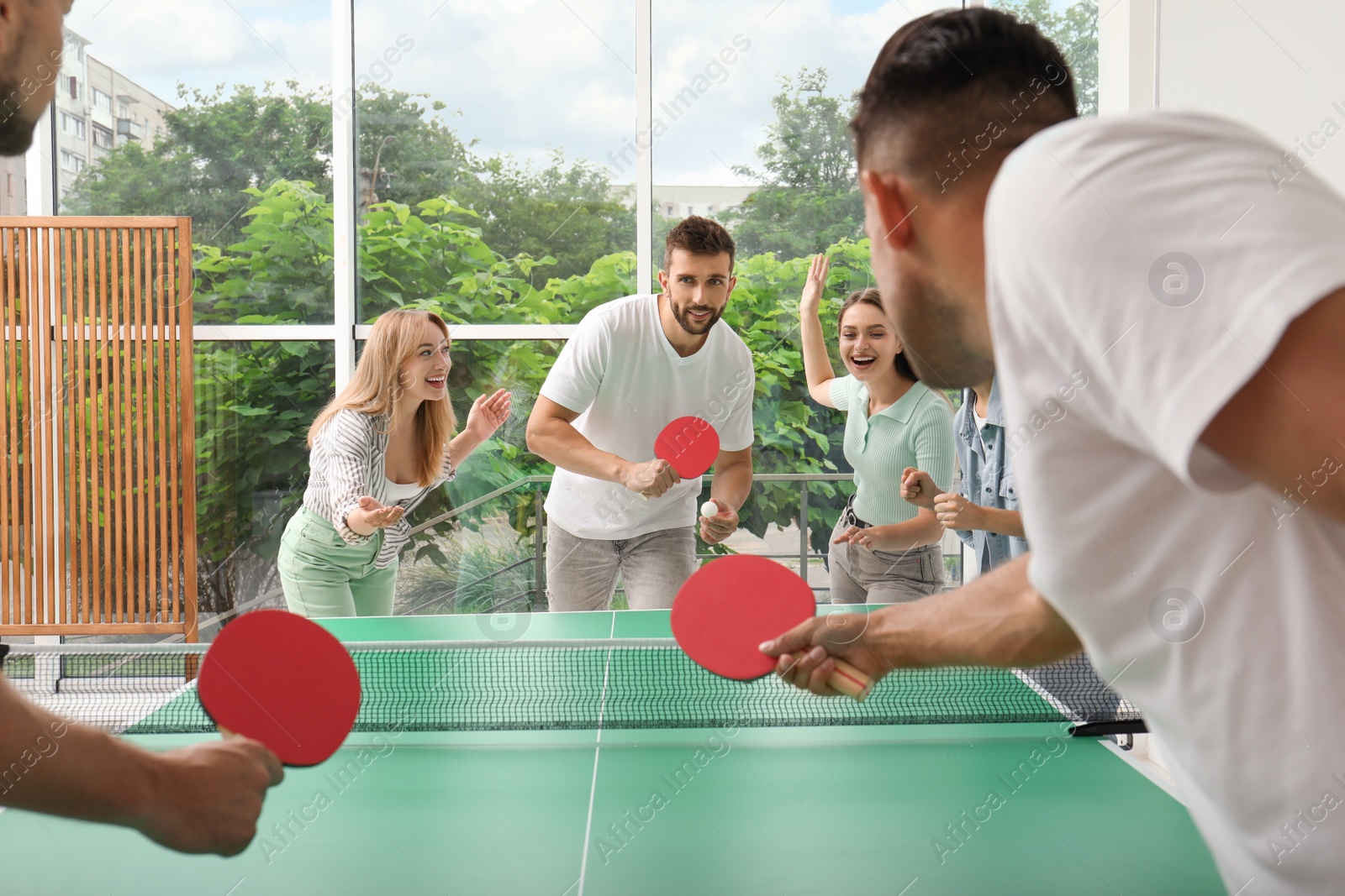 Photo of Happy friends playing ping pong together indoors