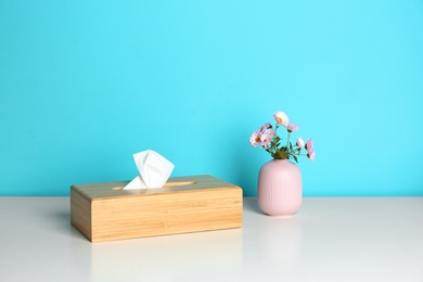 Wooden napkin holder with paper serviettes and flowers in small vase on table