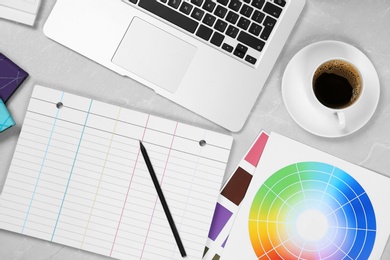 Photo of Flat lay composition with notebook, laptop and color palettes on light grey marble table. Designer's workplace