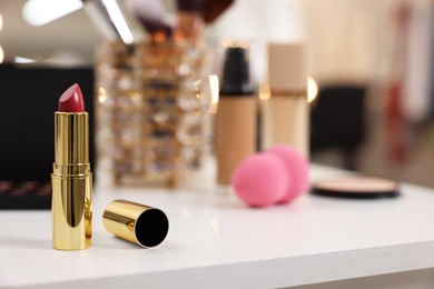 Red lipstick and other makeup products on white table indoors, selective focus