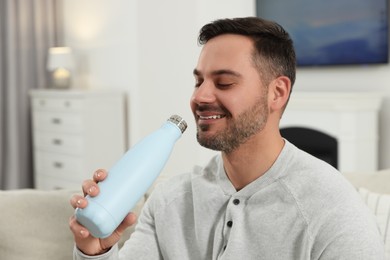 Photo of Man drinking from light blue thermo bottle indoors