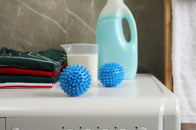 Blue dryer balls near stacked clean clothes and laundry detergents on washing machine