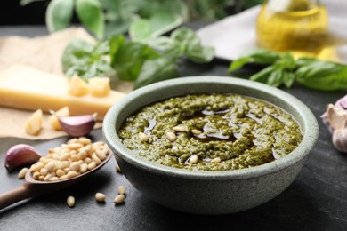 Photo of Tasty pesto sauce in bowl, pine nuts and garlic on black table, closeup