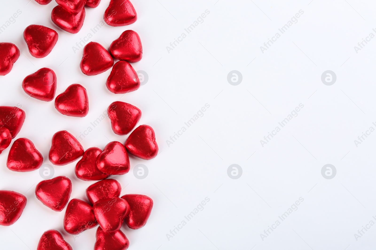 Photo of Heart shaped chocolate candies in red foil on white background, top view