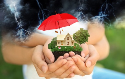 Image of Insurance concept - umbrella demonstrating protection. Family holding house model with green lawn, closeup