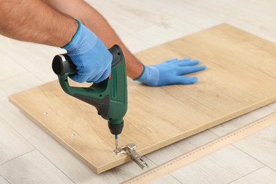 Photo of Man with electric screwdriver assembling furniture on floor, closeup