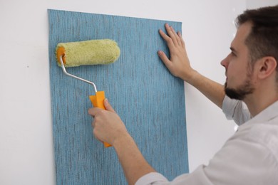 Man hanging light blue wallpaper in room