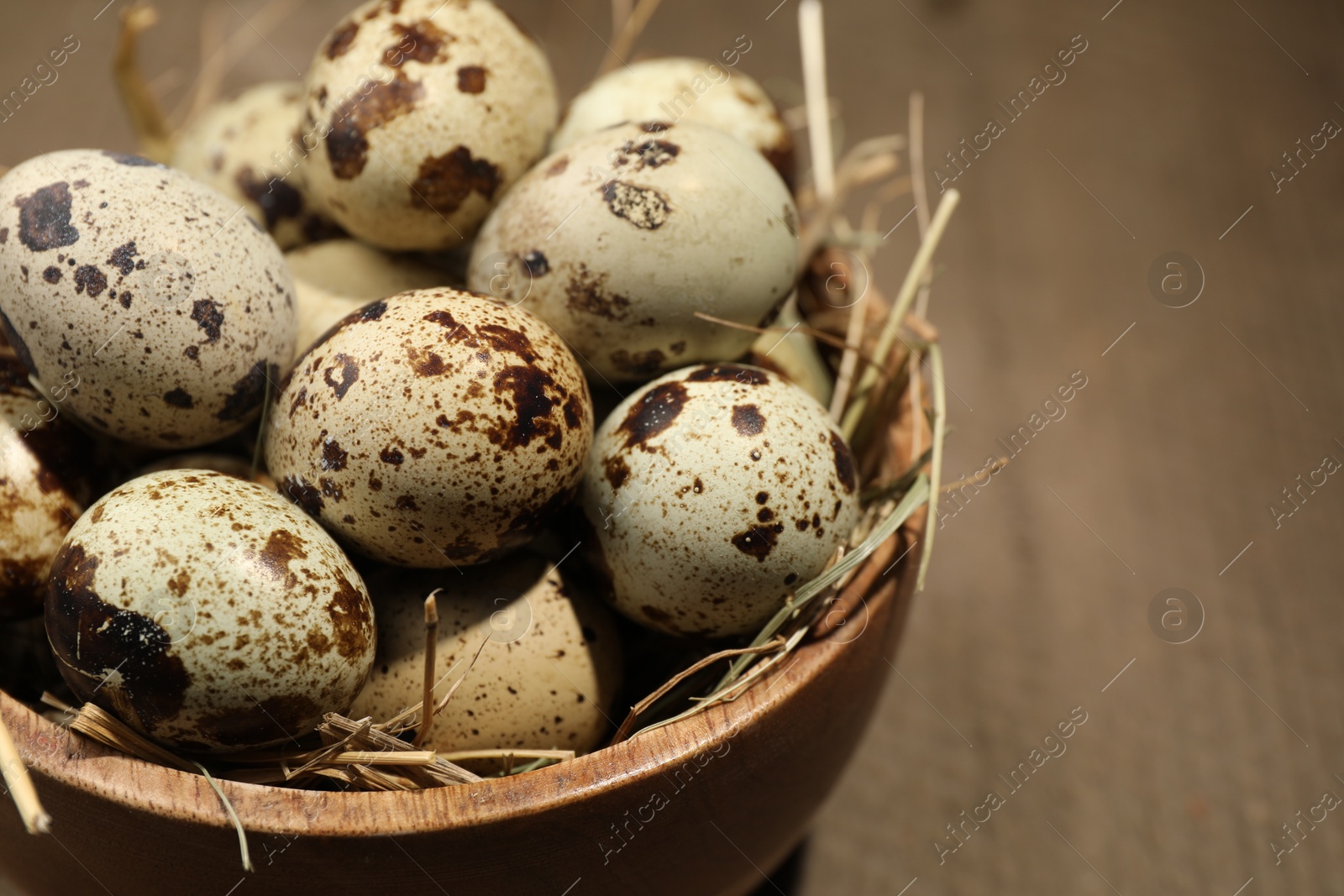 Photo of Wooden bowl with quail eggs and straw on table, closeup. Space for text