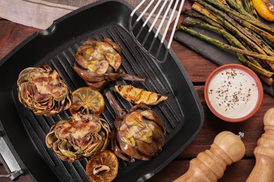 Photo of Tasty grilled artichokes with sauce on wooden table, flat lay