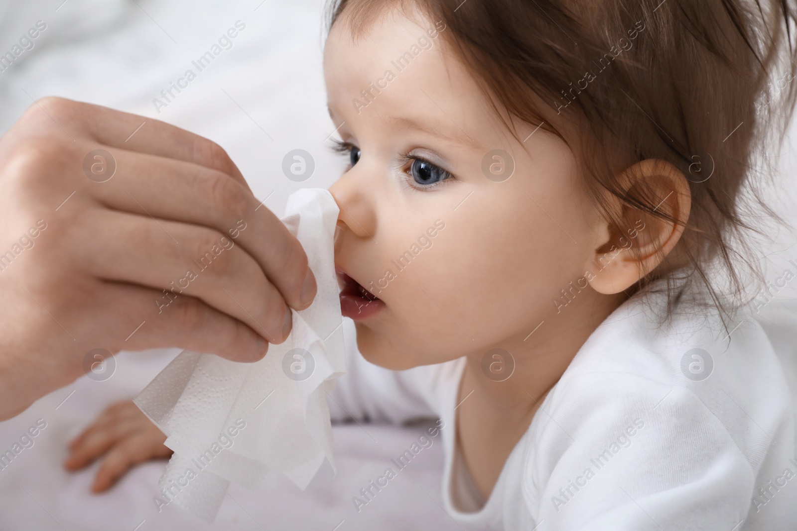 Photo of Father taking care of little baby suffering from runny nose in bed, closeup