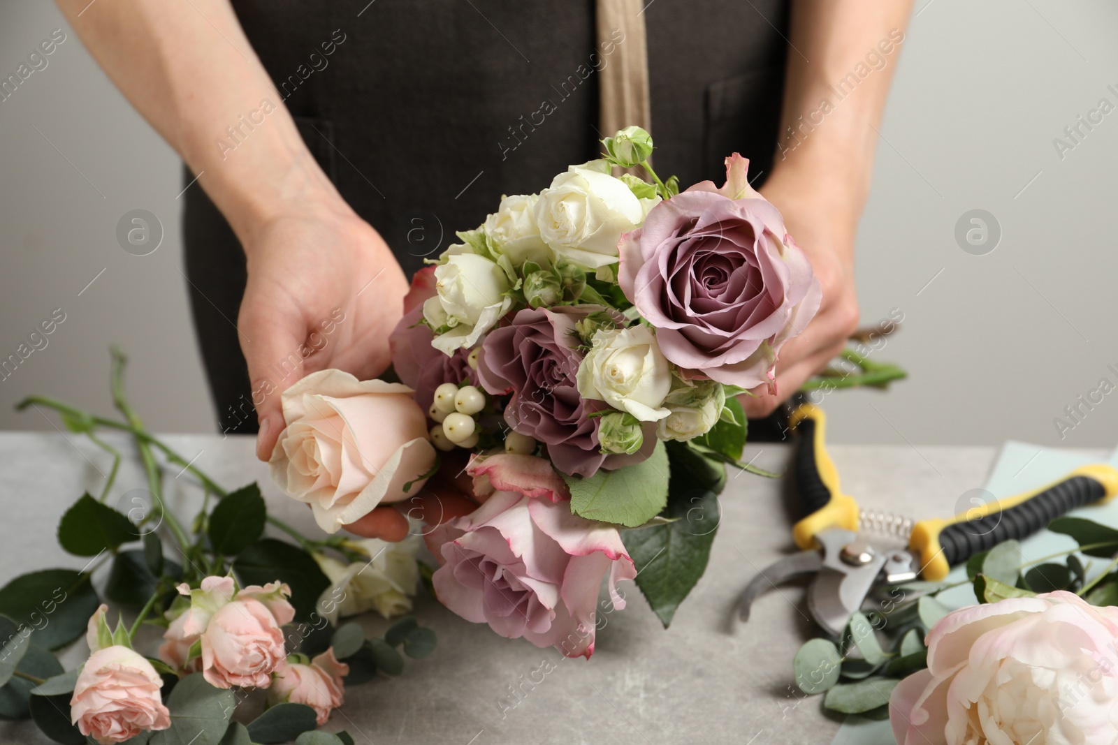 Photo of Florist creating beautiful bouquet at grey table against light background, closeup