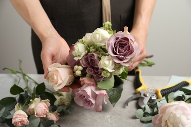 Photo of Florist creating beautiful bouquet at grey table against light background, closeup