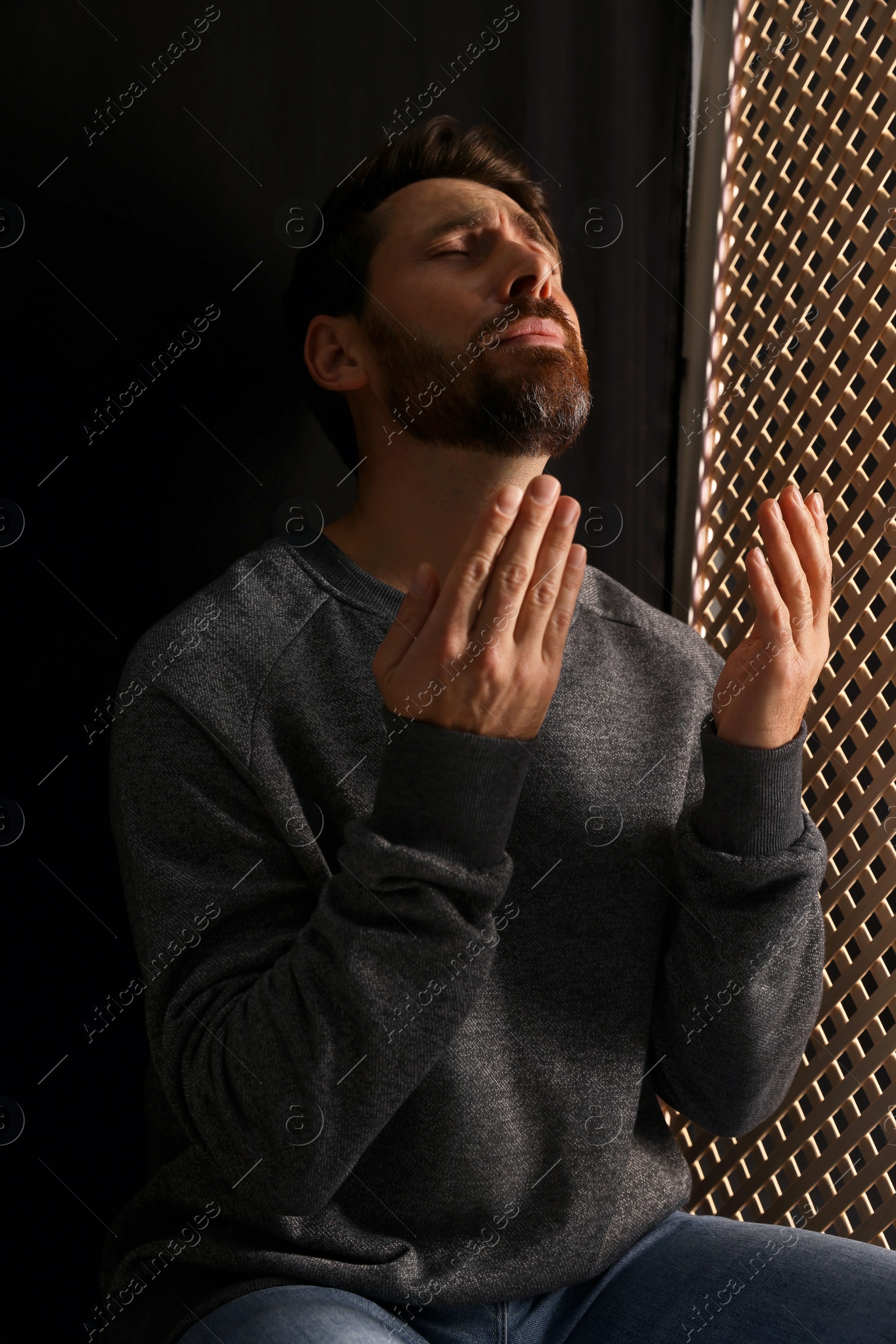 Photo of Upset man praying to God during confession in booth