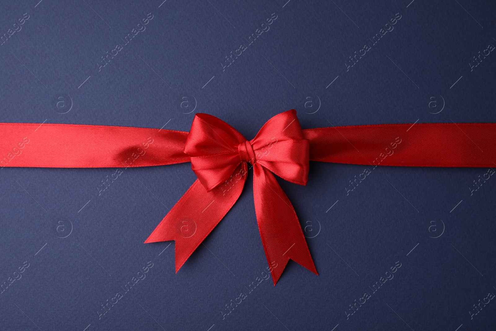 Photo of Red satin ribbon with bow on blue background, top view