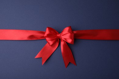 Photo of Red satin ribbon with bow on blue background, top view