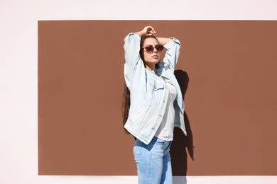 Photo of Young hipster woman in stylish jeans and jacket posing near color wall