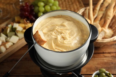 Photo of Fondue with tasty melted cheese, fork and different snacks on wooden table