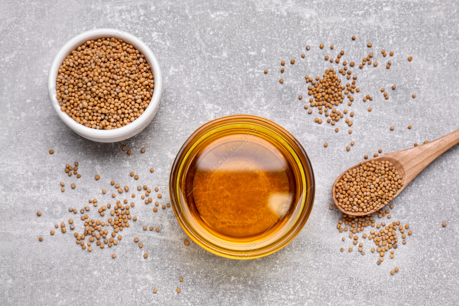 Bowl of natural oil and mustard seeds on light grey table, flat lay Photo of Bowl of natural oil and mustard seeds on light grey table, flat lay