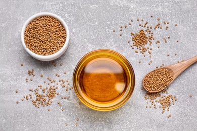 Photo of Bowl of natural oil and mustard seeds on light grey table, flat lay