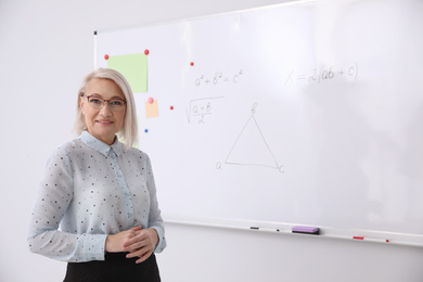 Mature teacher near whiteboard in modern classroom. Space for text