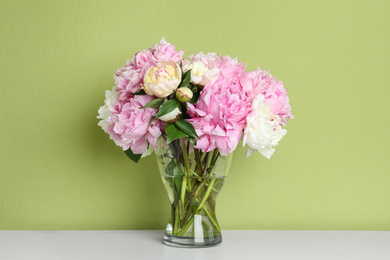 Photo of Beautiful peonies on white table against green background