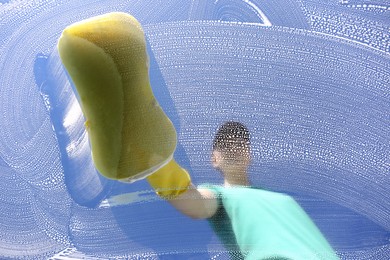 Woman cleaning glass with sponge on sunny day