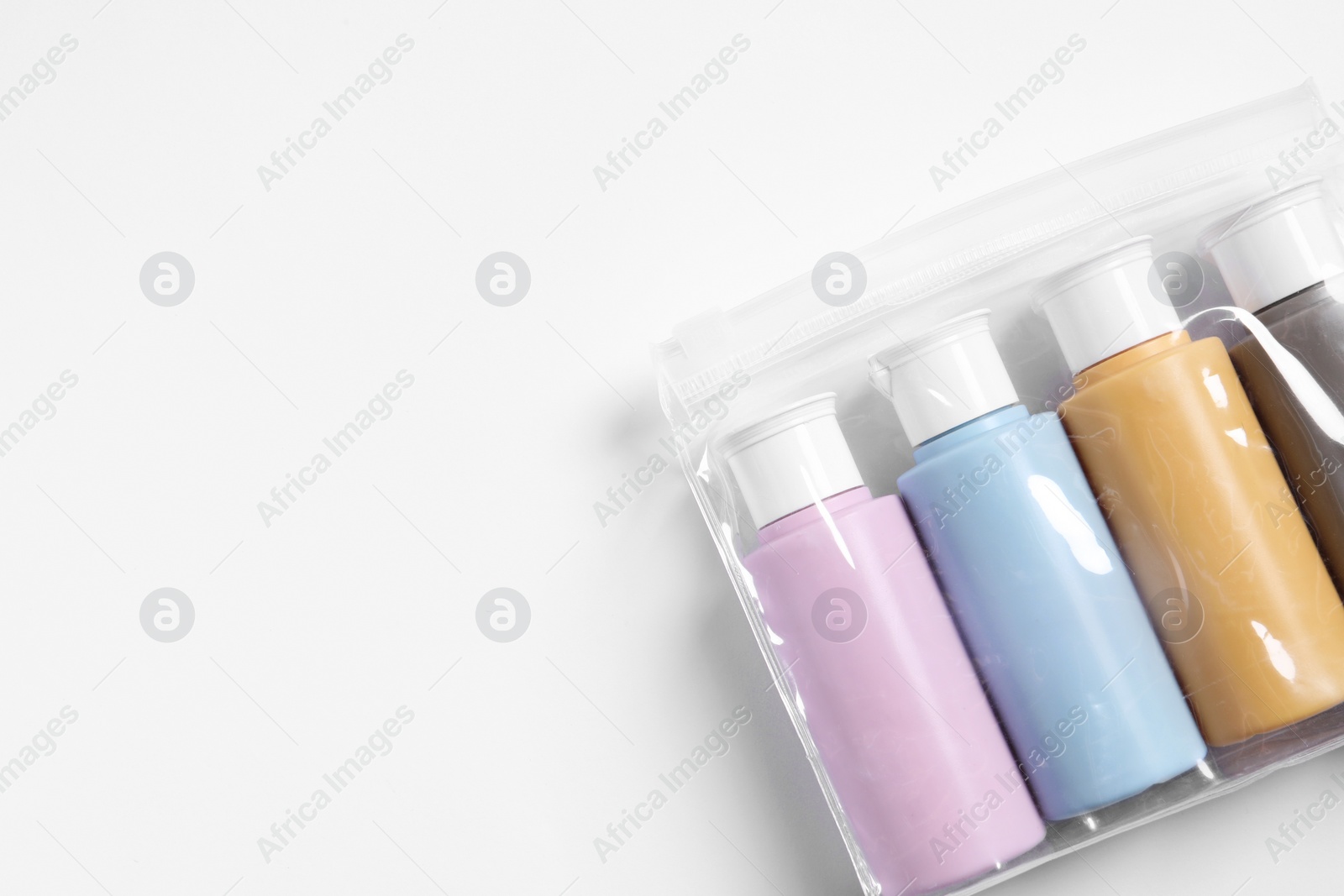 Photo of Cosmetic travel kit in plastic bag on white background, top view. Space for text