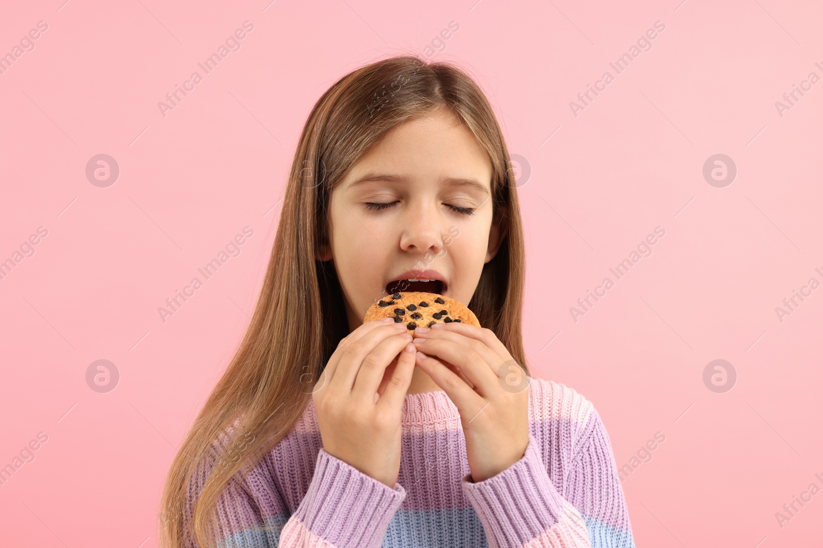 Photo of Cute girl eating chocolate chip cookie on pink background