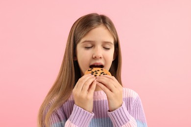 Photo of Cute girl eating chocolate chip cookie on pink background