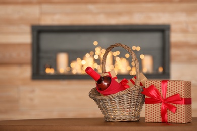 Photo of Wicker basket with bottle of wine and gift boxes on table in room. Space for text