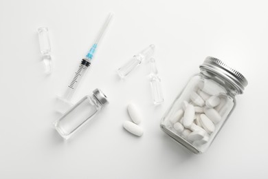 Photo of Glass ampoules with liquid, pills and syringe on white background, flat lay