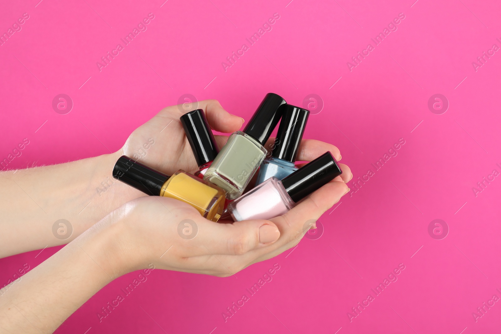 Photo of Woman holding nail polishes on pink background, closeup