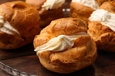 Delicious profiteroles with cream filling on wooden table, closeup