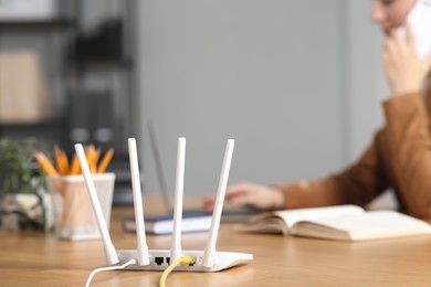 Photo of Woman talking on phone while working with laptop at table indoors, focus on Wi-Fi router