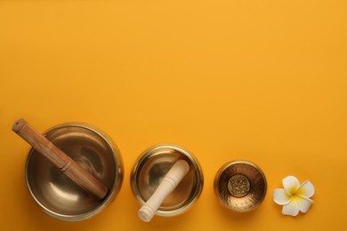 Golden singing bowls, mallets and flower on orange background, flat lay. Space for text